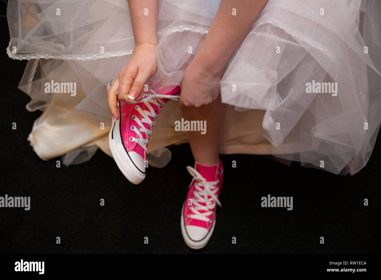Sposa a mettere su e allacciatura sneakers rosa su piedi Foto Stock
