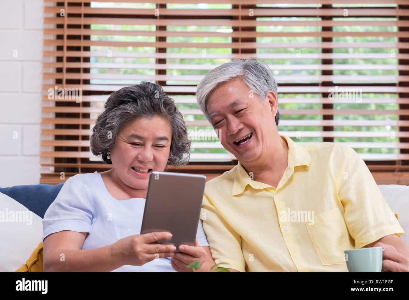 Asian senior giovane impara a utilizzando la tabella compute sul divano nel soggiorno di casa.senior con la tecnologia lfiestyle.invecchiamento a home concetto Foto Stock