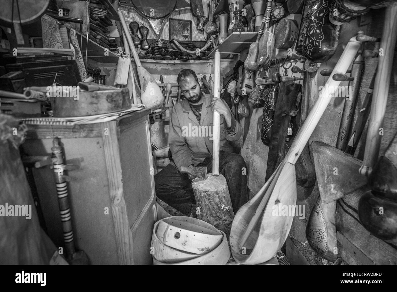 Merchant si ritaglia un pezzo di legno in post nel suo negozio di fronte al quartiere della medina di Marrekech, Marocco Foto Stock