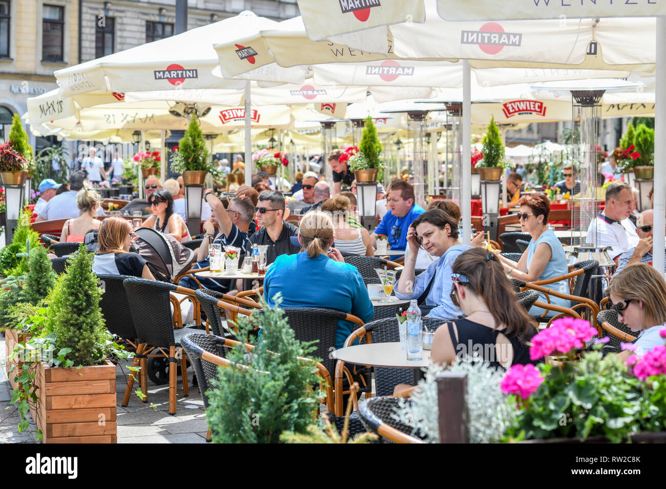 Persone sedute e mangiare all'aperto tavoli da pranzo con coperchio ombrello nella Piazza del Mercato di Cracovia-w Città Vecchia, Piccola Polonia voivodato, Polonia. Foto Stock