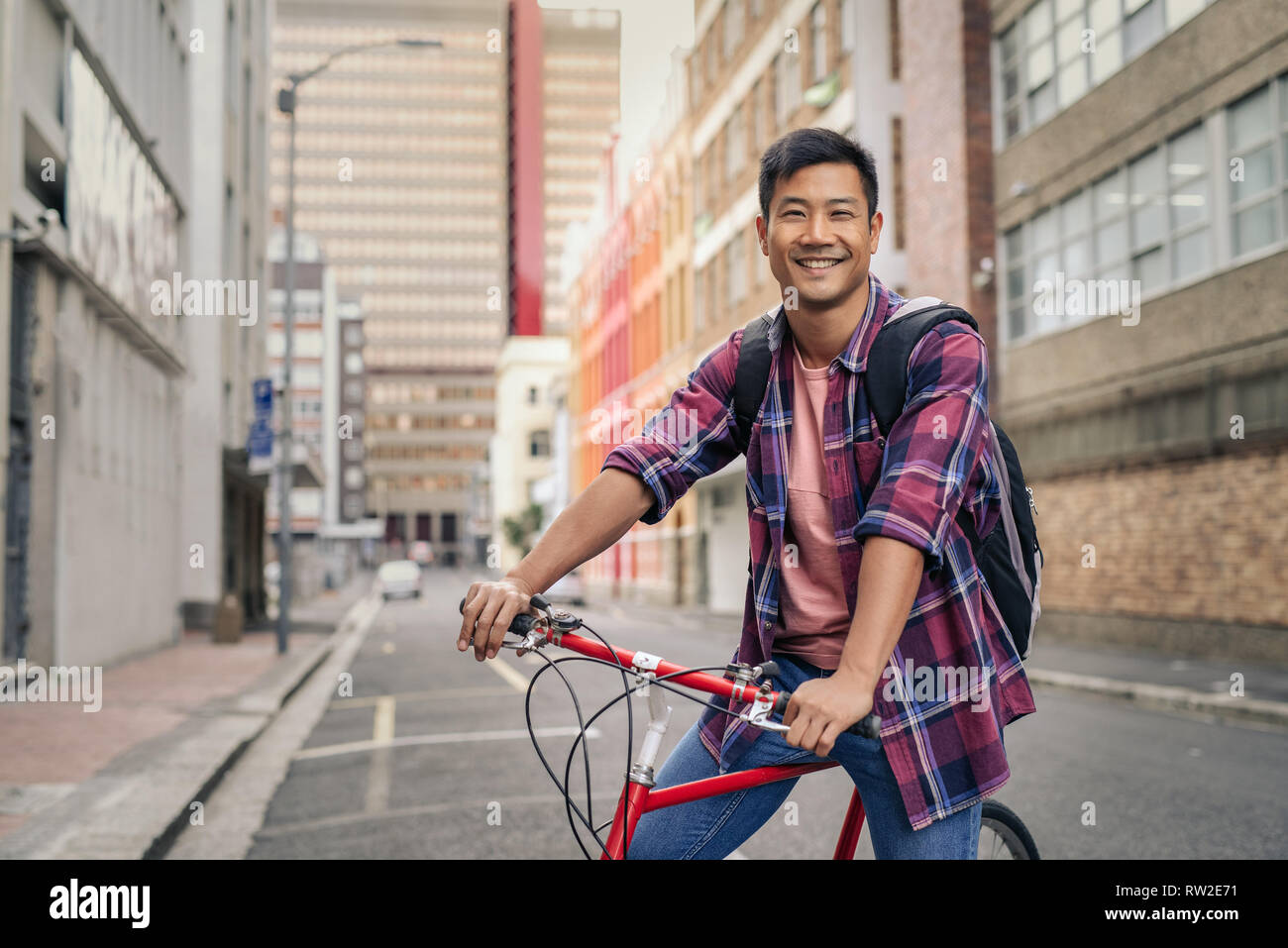 Uomo sorridente in piedi con la sua bicicletta su una strada di città Foto Stock