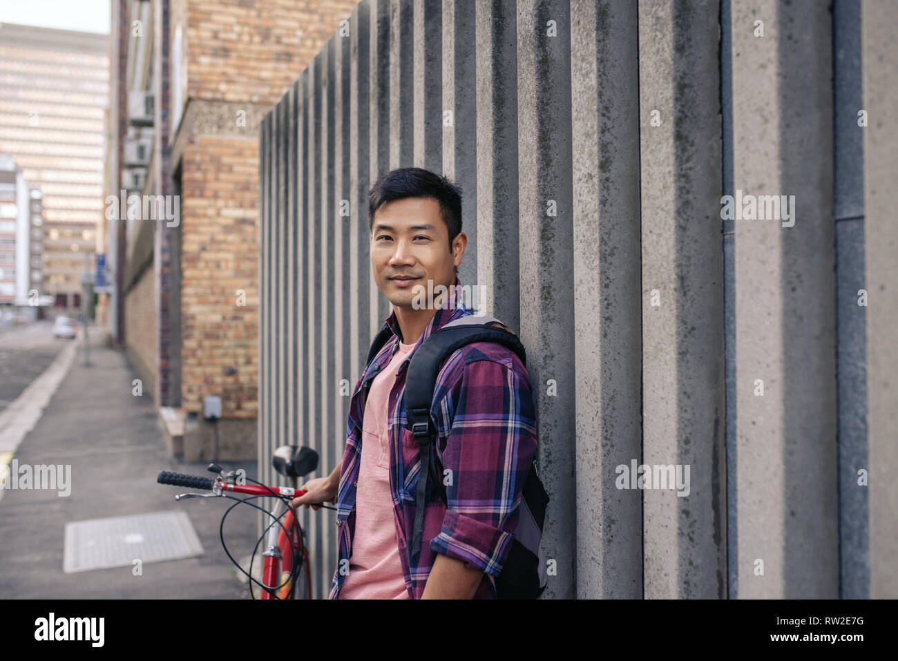 Sorridente giovane uomo appoggiato contro un muro con la sua moto Foto Stock