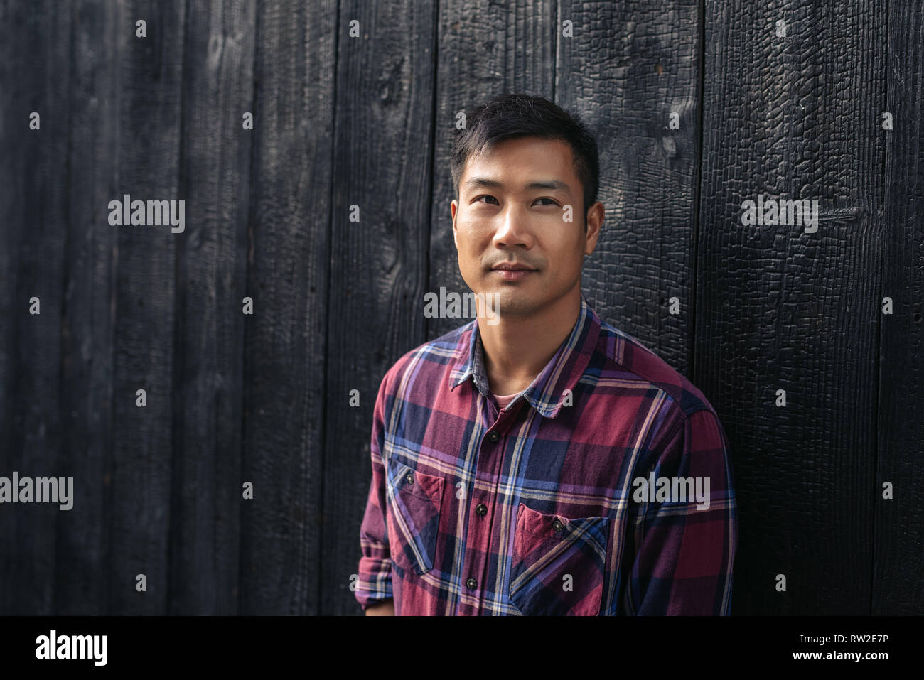 Fiducioso giovane uomo asiatico in piedi da una parete scura al di fuori Foto Stock
