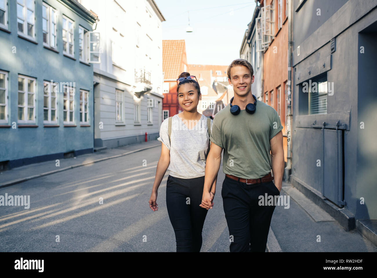 Coppia giovane sorridere mentre passeggiate in città tenendo le mani Foto Stock