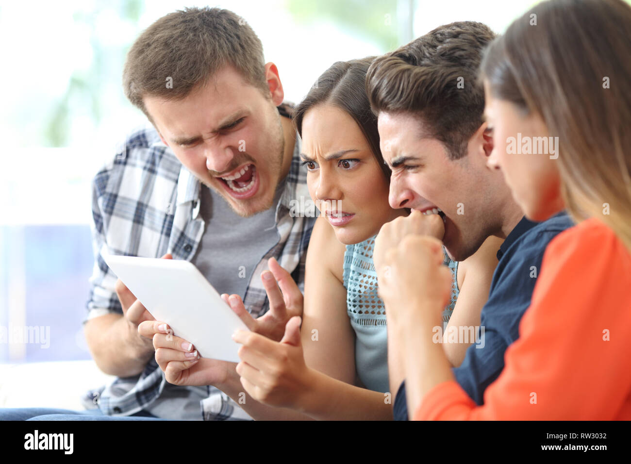 Arrabbiato gruppo di amici guardare i media su tablet seduta su un divano nel salotto di casa Foto Stock