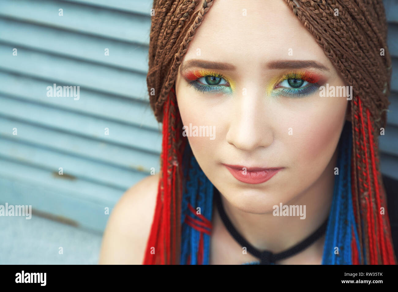 Giovane donna con il trucco luminoso e colorato cornrows Foto Stock