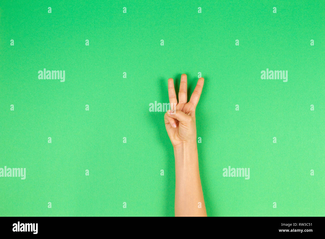 Kid mano che mostra tre dita su sfondo verde Foto Stock