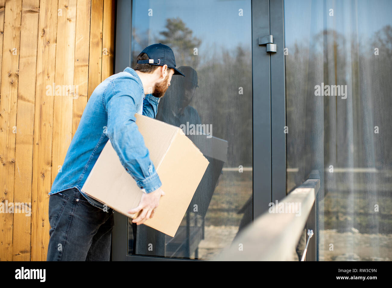 Consegna uomo cerca all'interno della casa moderna, offrendo alcune merci in il pacco di carta Foto Stock