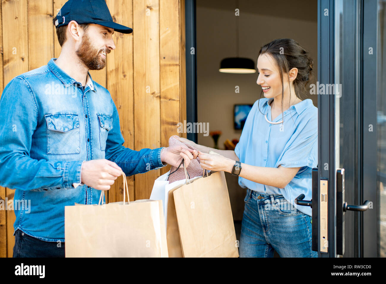 Uomo di consegna portando un po' di merci imballate in sacchi di carta per  una giovane donna client a casa. Acquistare vestiti online e concetto di  consegna Foto stock - Alamy