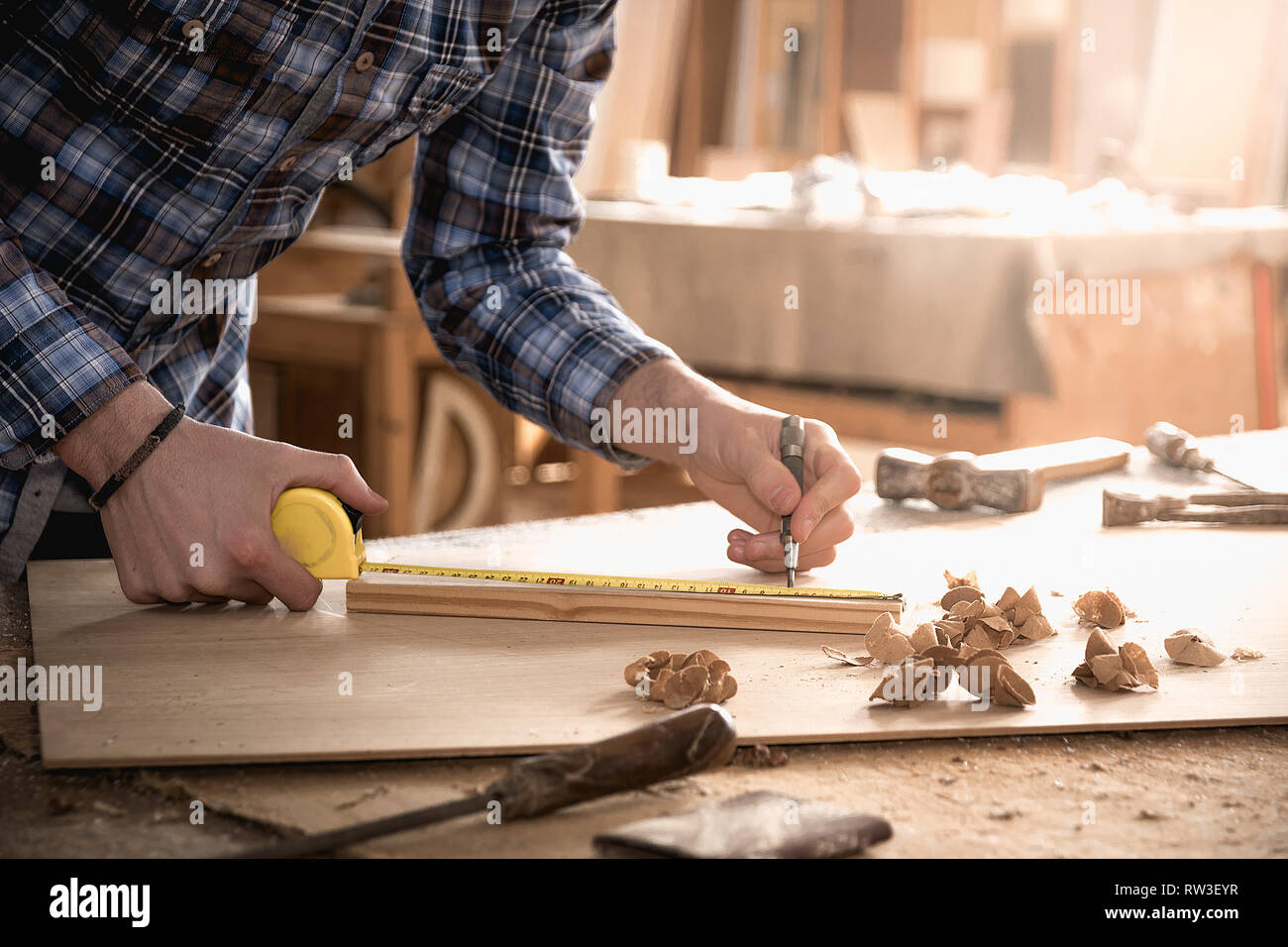 Carpenter lavora con metro a nastro, il metro o la regola di prendere misure di legno utilizzando una matita. Workshop sullo sfondo. Carpenter workbench. Foto Stock