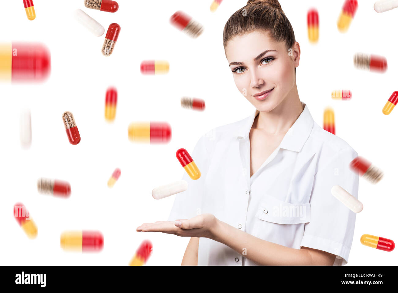 Giovane medico donna in piedi tra pillole pioggia su sfondo bianco. Foto Stock