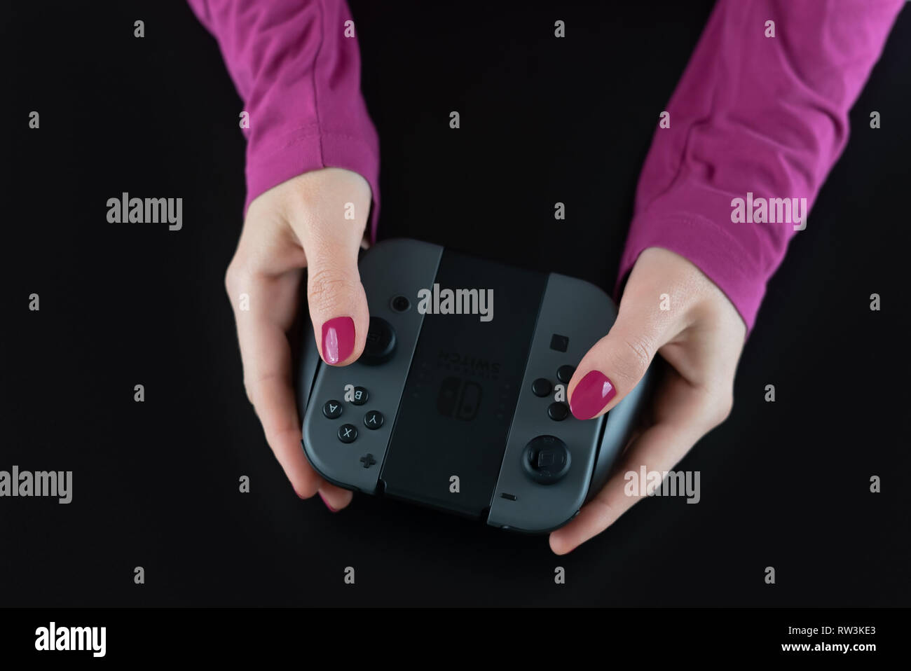Vista superiore della donna le mani con rosa smalto per unghie sulle dita tenendo premuto un interruttore Nintendo controller di gioco per la riproduzione di video digitali isolati giochi su nero Foto Stock