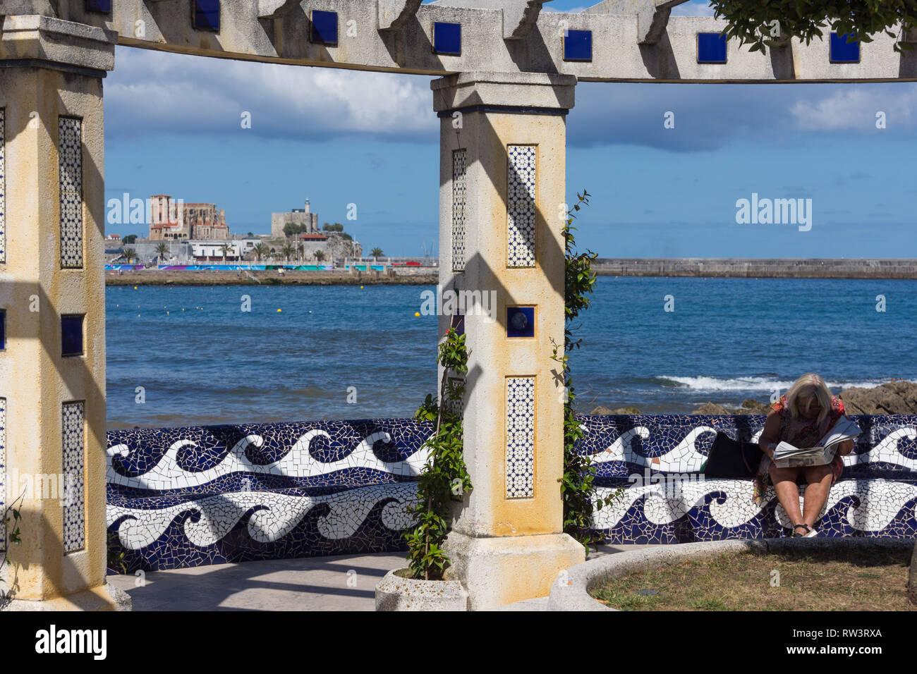 Lettura di un quotidiano in ombra dal brazo Mar beach in Castro Urdiales con la Chiesa di Santa María de la Asunción in background Foto Stock