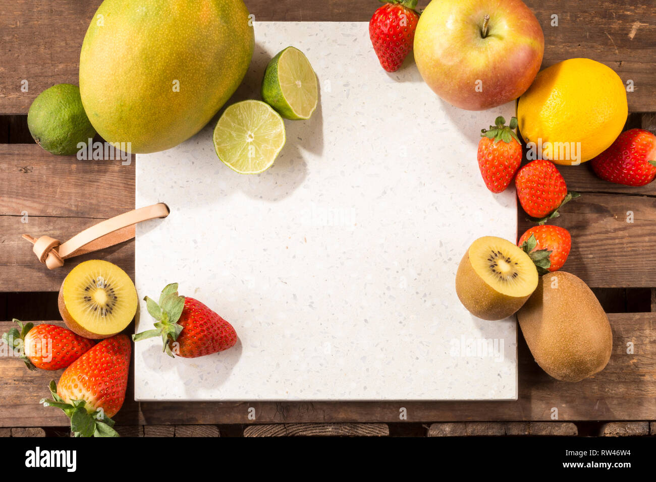 Pietra di calcestruzzo server con spazio per il testo su un legno rustico listone superficie. e disposti frutti. Apple, limone, fragole, kiwi, tigli e mango. Foto Stock