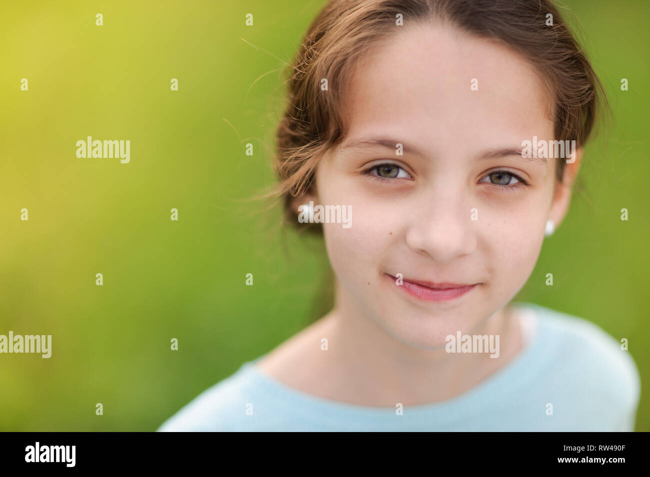 Closeup ritratto di sorridenti poco ragazza caucasica in orecchini e camicetta blu sul caldo sfondo verde Foto Stock