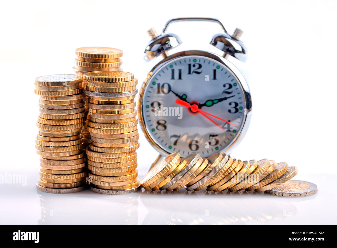 Un sacco di monete metalliche in euro a fronte di un orologio sveglia isolato su bianco. Foto Stock
