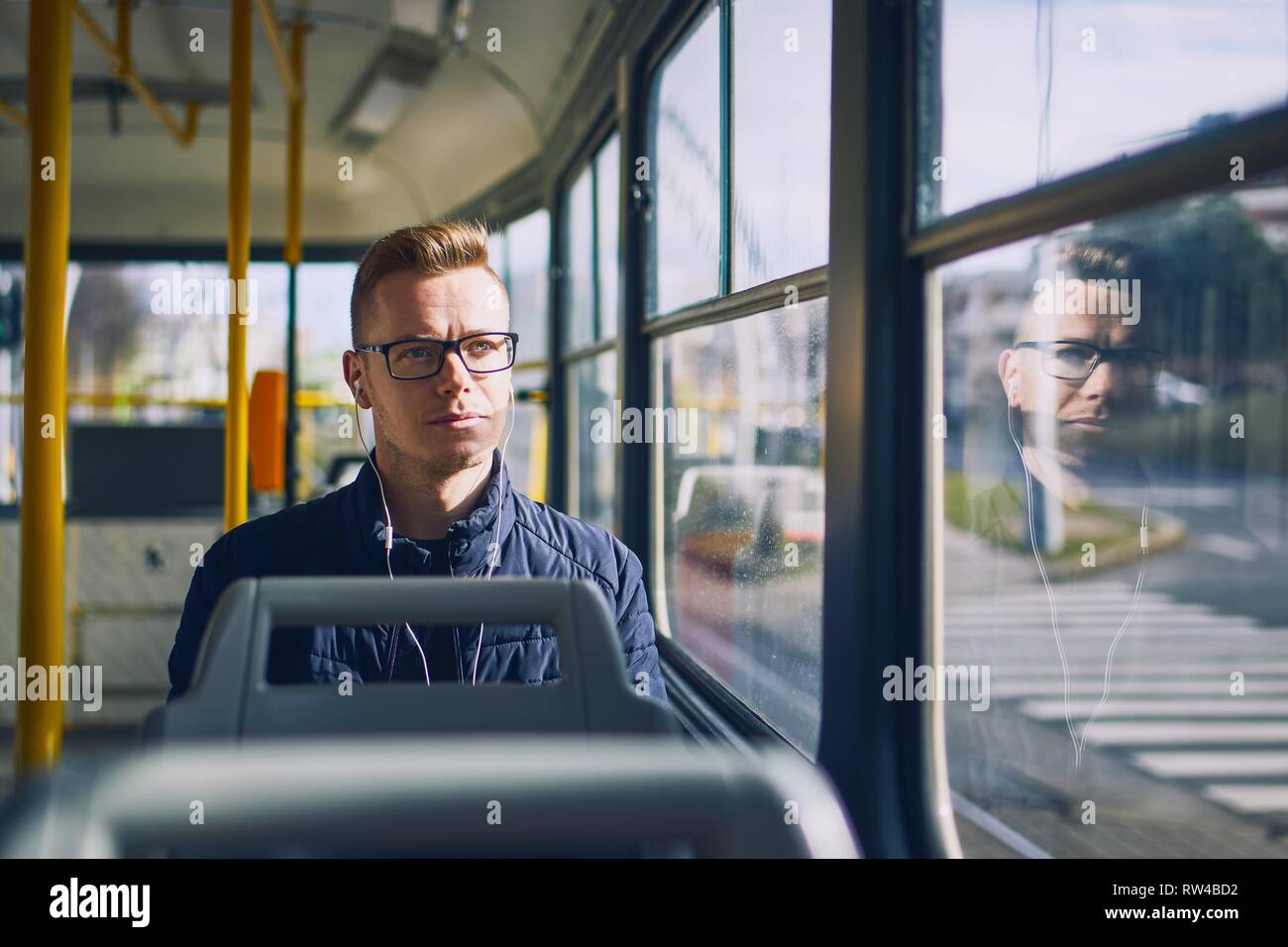 Giovane uomo che ascolta musica in tram. Viaggiare con i mezzi di trasporto pubblici. Foto Stock