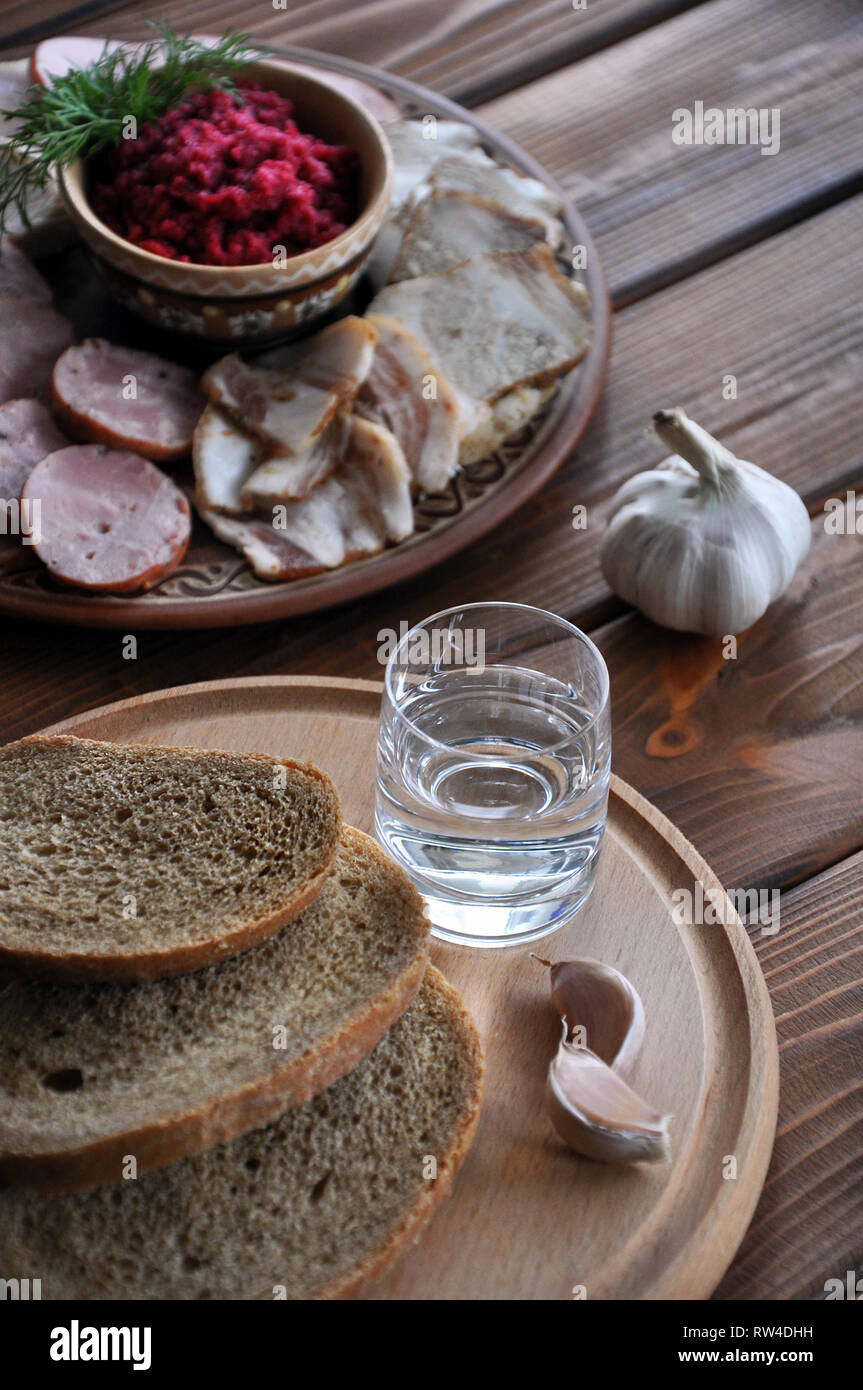 Un bicchiere di vodka con pane di segale e aglio sul round piatto in legno con moresnack sullo sfondo sfocato, il fuoco selettivo Foto Stock