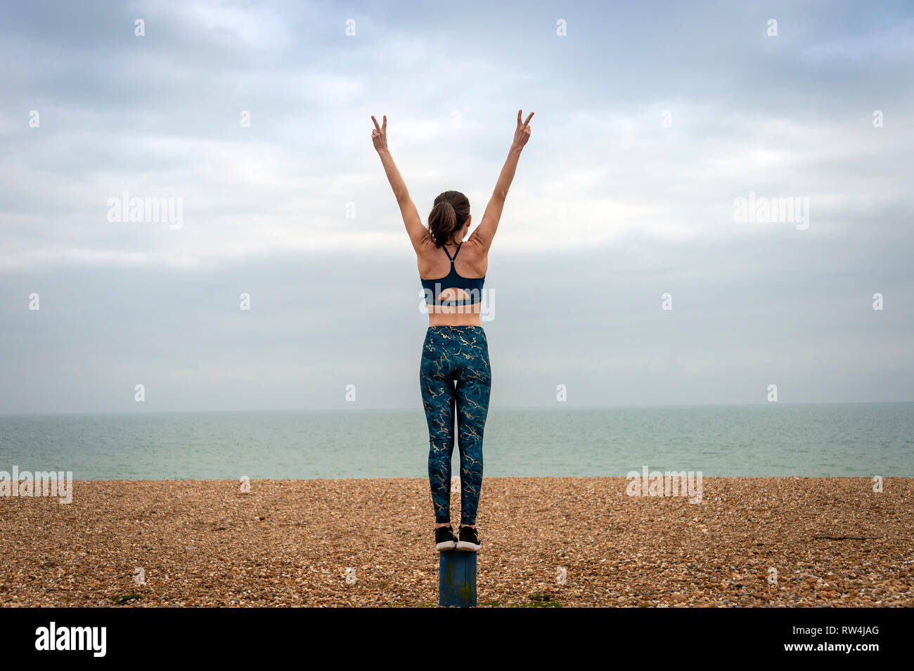 Donna in piedi con le braccia sollevate sulla spiaggia, vista posteriore, copyspace Foto Stock