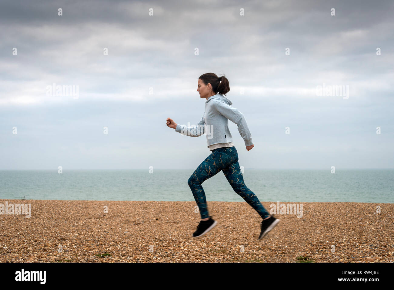 Donna che corre lungo la spiaggia di ghiaia dal mare, mantenersi in forma. Foto Stock