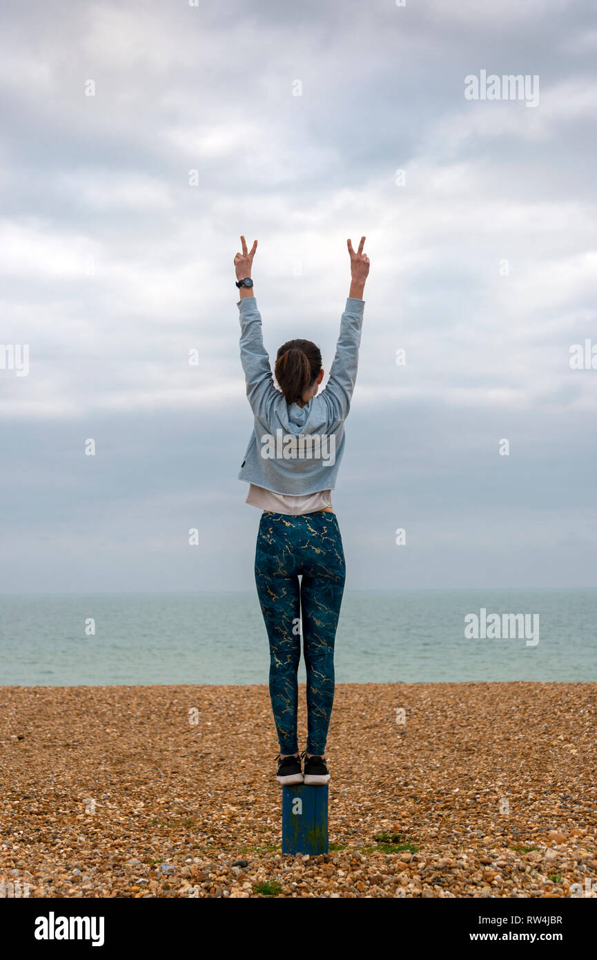 Donna in piedi con le braccia sollevate sulla spiaggia, vista posteriore, copyspace Foto Stock