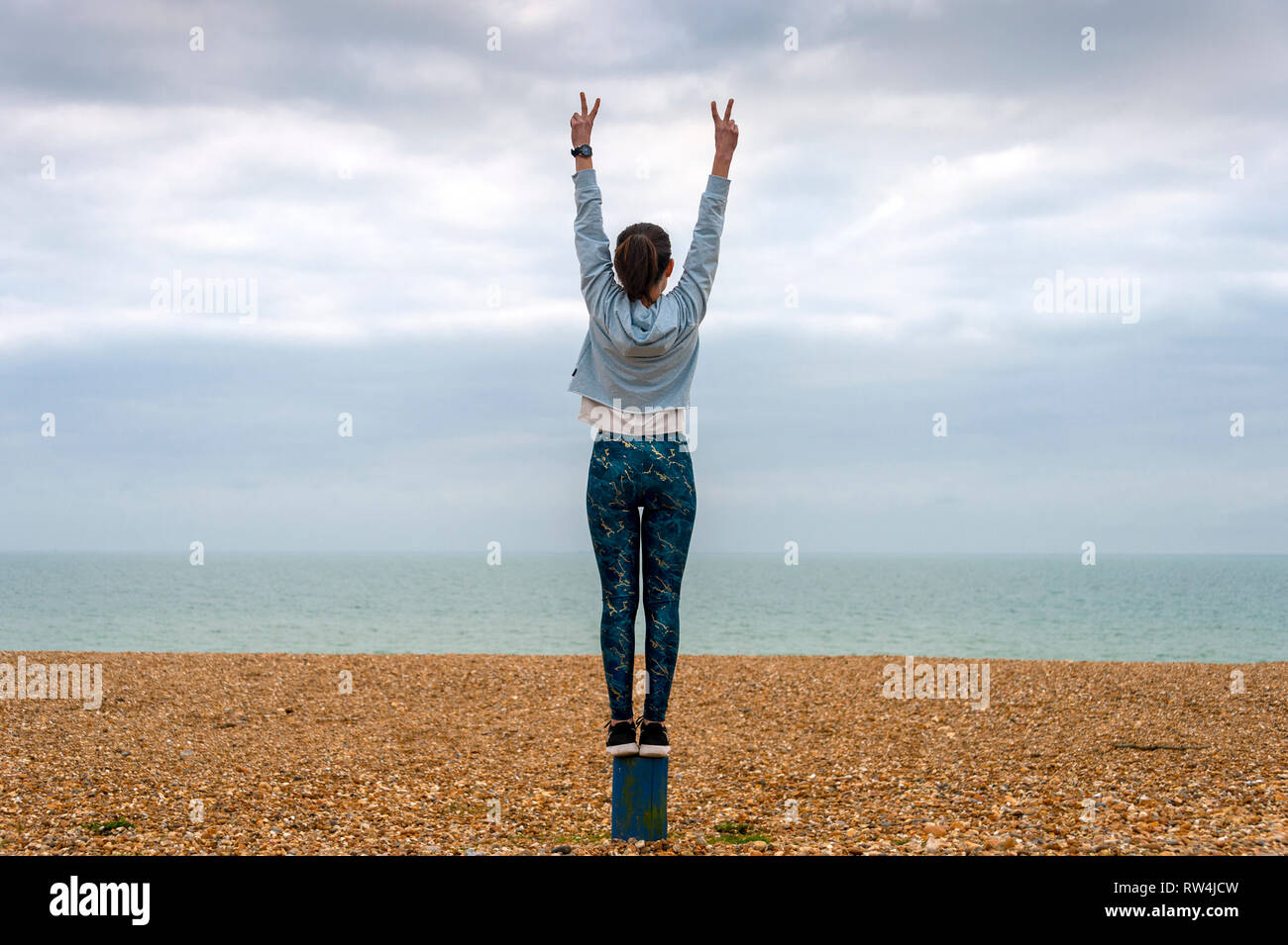 Donna in piedi con le braccia sollevate sulla spiaggia, vista posteriore, copyspace Foto Stock