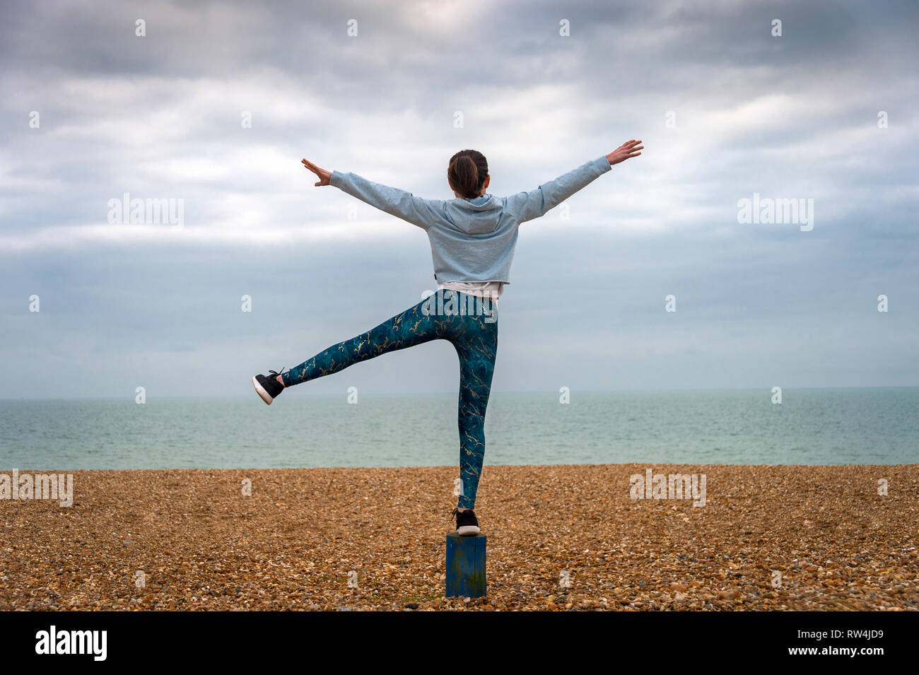 Donna in piedi con le braccia sollevate sulla spiaggia, vista posteriore, copyspace Foto Stock