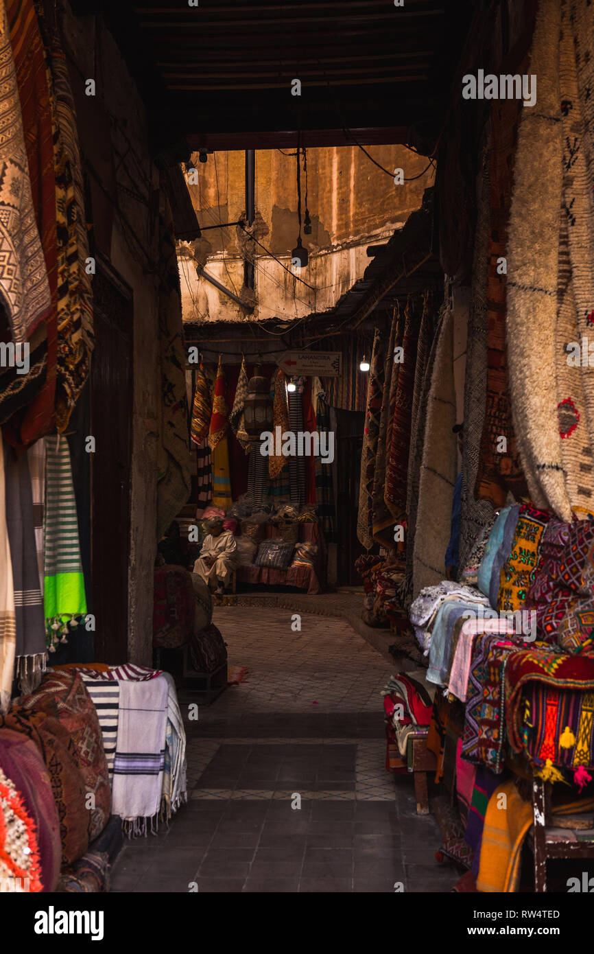 Tipico vicolo marocchino nel Souk della Medina di Marrakech con una varietà di sciarpe e altri prodotti di tessitura (Marrakech, Marocco, Africa) Foto Stock