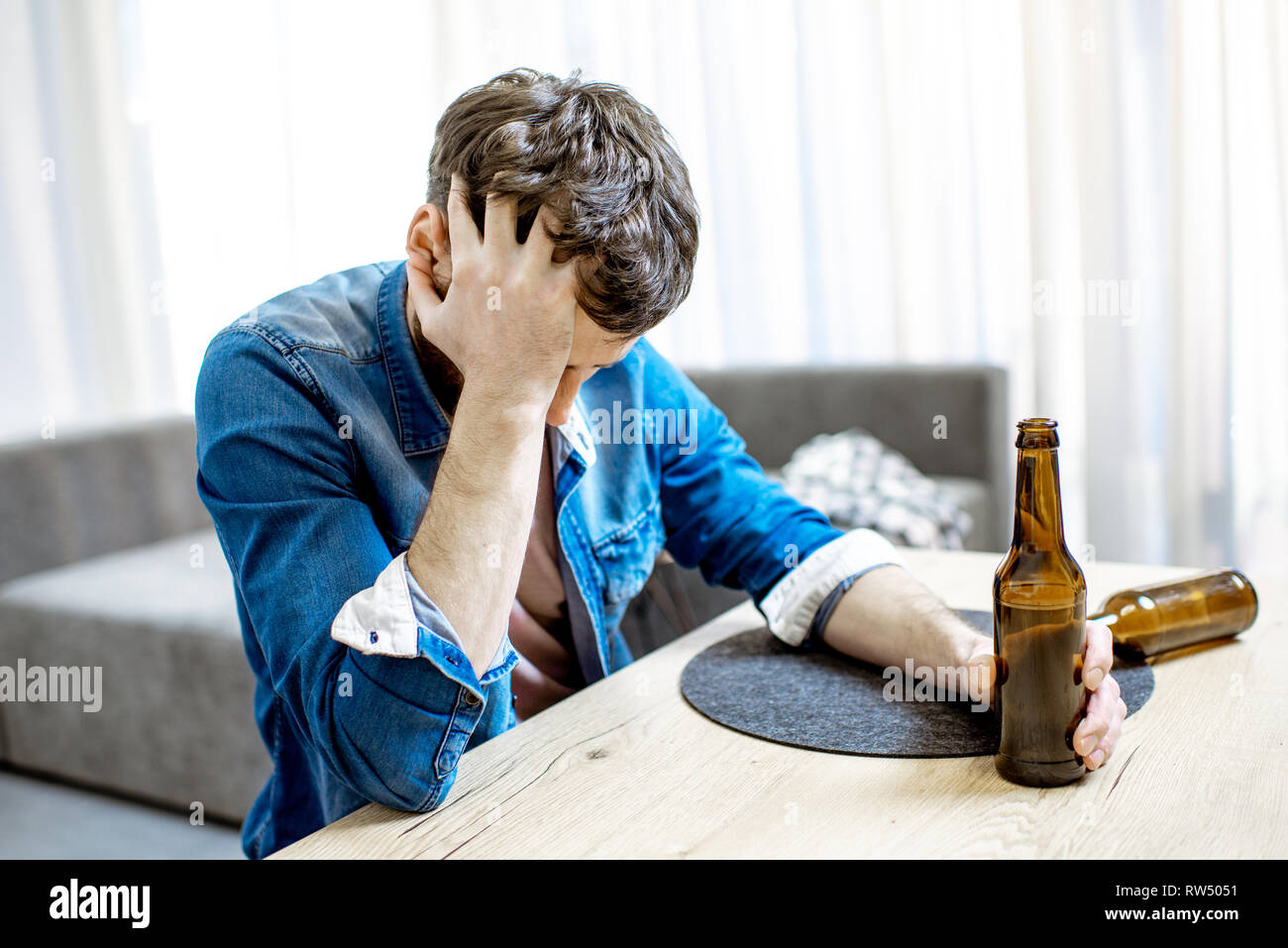 Bevuto alcolici maschile seduto con bottiglie sentirsi depressi e che soffrono di mal di testa a casa Foto Stock
