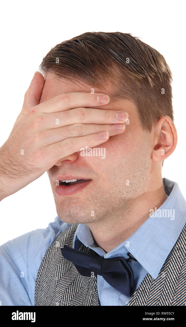 Un giovane uomo bello stare in un giubbotto grigio e il filtro bow tie, tenendo una mano sopra i suoi occhi si vergogna, isolato per sfondo bianco Foto Stock