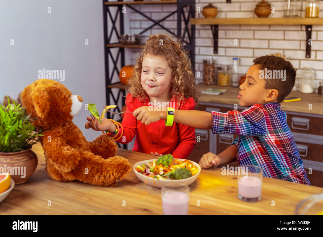 Positivo felici i bambini alimentando il loro giocattolo bear Foto Stock