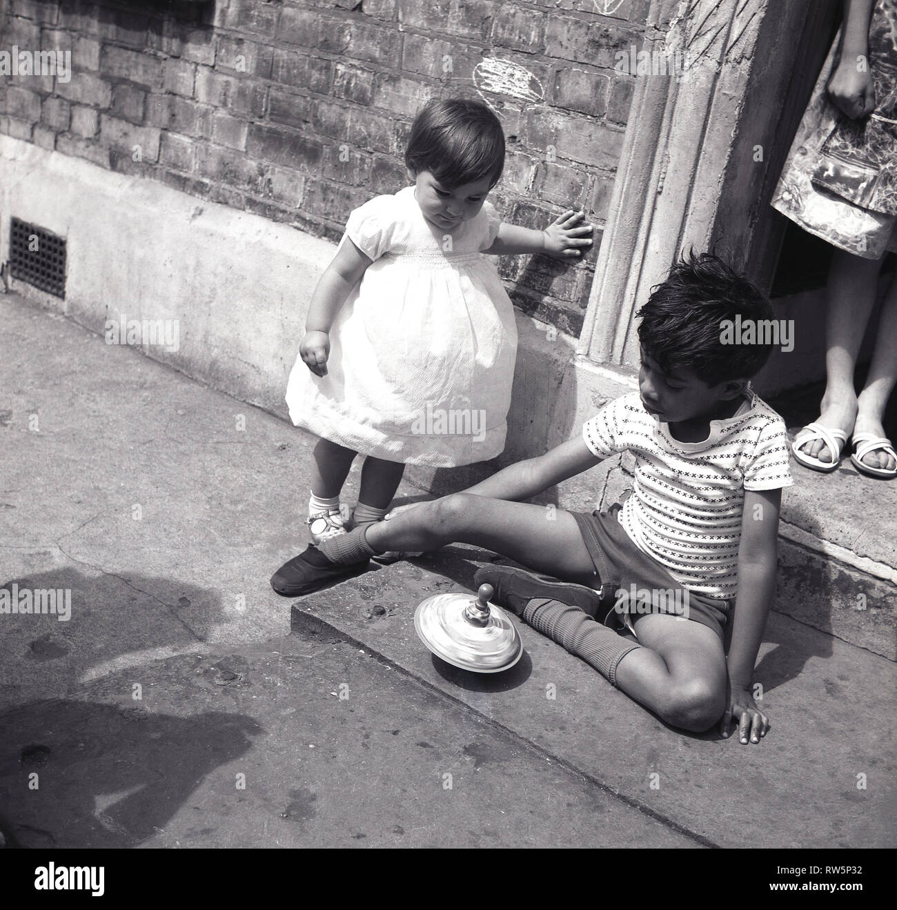 Anni sessanta, all interno della città vivere....un giovane ragazzo con sua sorella guardando, giocando con un giocattolo di filatura al di fuori sulla soglia di casa sua, Camden Town, Londra, Inghilterra, Regno Unito. Foto Stock