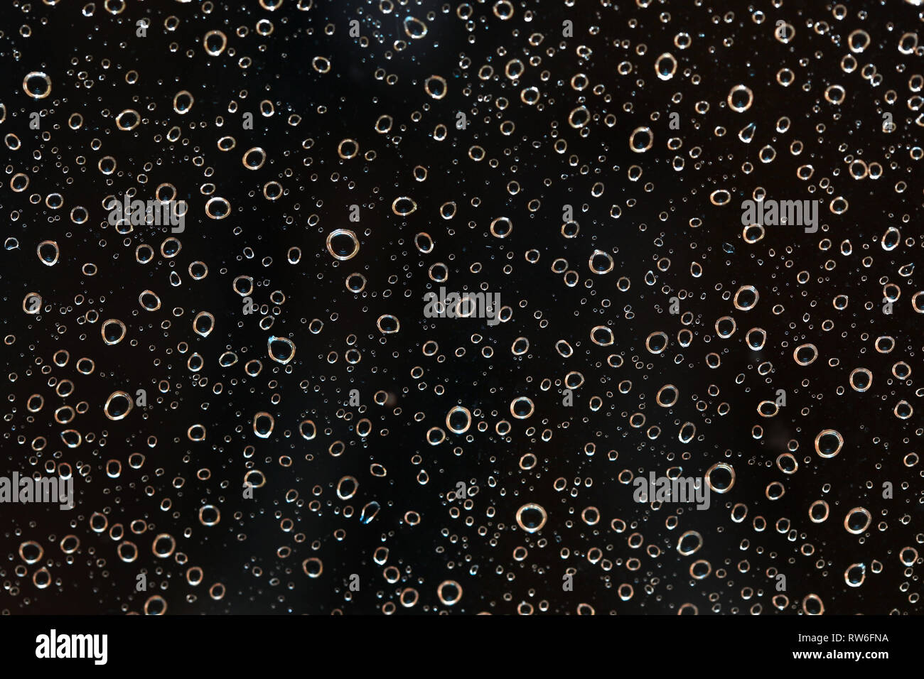 Primo piano della pioggia di gocce d'acqua dietro il vetro alla sera. Sembra che bolle nel liquido nero. Abstract sfondo umido. Foto Stock