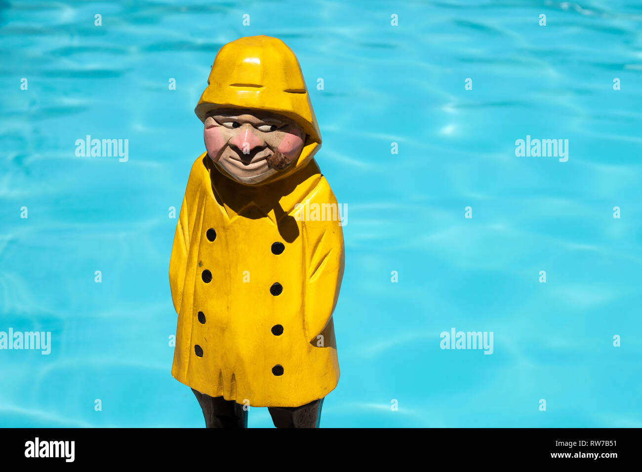Pescatore figura in legno di colore giallo con la pioggia e il cappotto di tubo di fumo sulla piscina dello sfondo. Spazio di copia Foto Stock