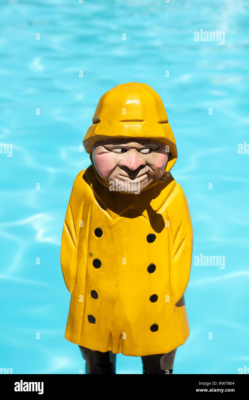 Pescatore figura in legno di colore giallo con la pioggia e il cappotto di tubo di fumo sulla piscina sullo sfondo Foto Stock