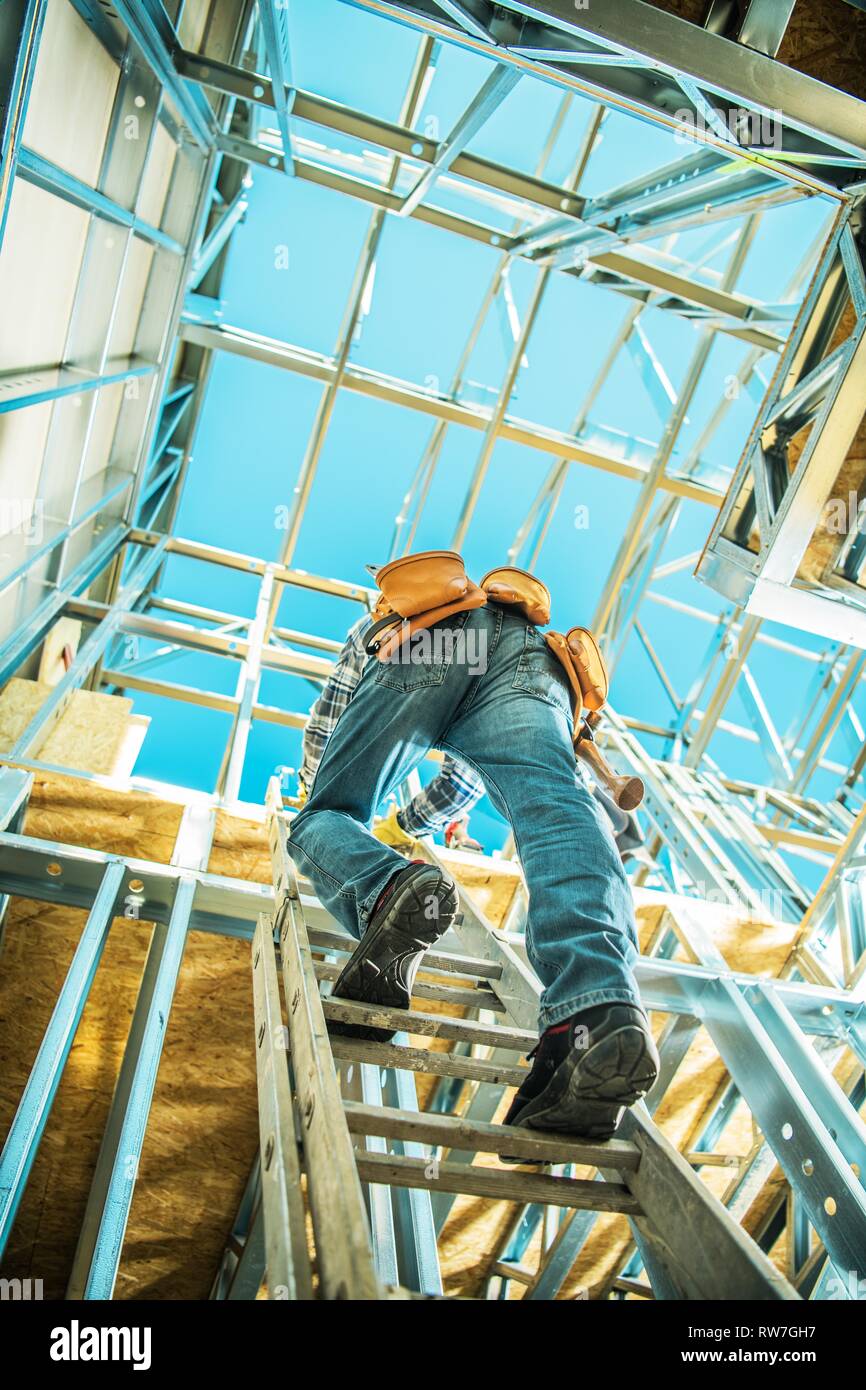 Lavoratore su una scala che va al piano superiore della casa sviluppati. Lo scheletro di edificio in acciaio costruzione lavoro. Foto Stock