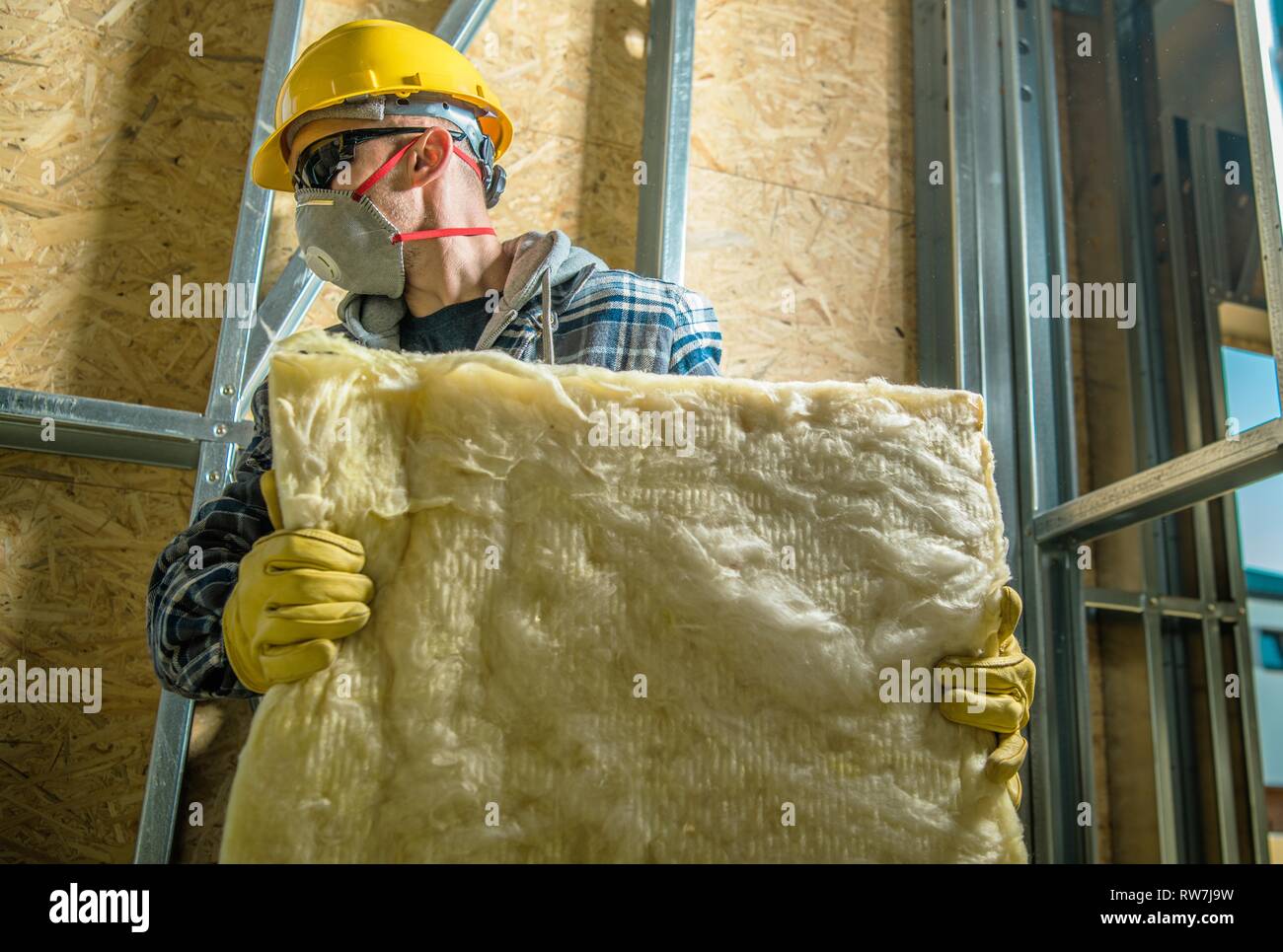 Costruzione caucasica Lavoratore che indossa la maschera di sicurezza il movimento dei pezzi di coibentazione in lana minerale. Foto Stock