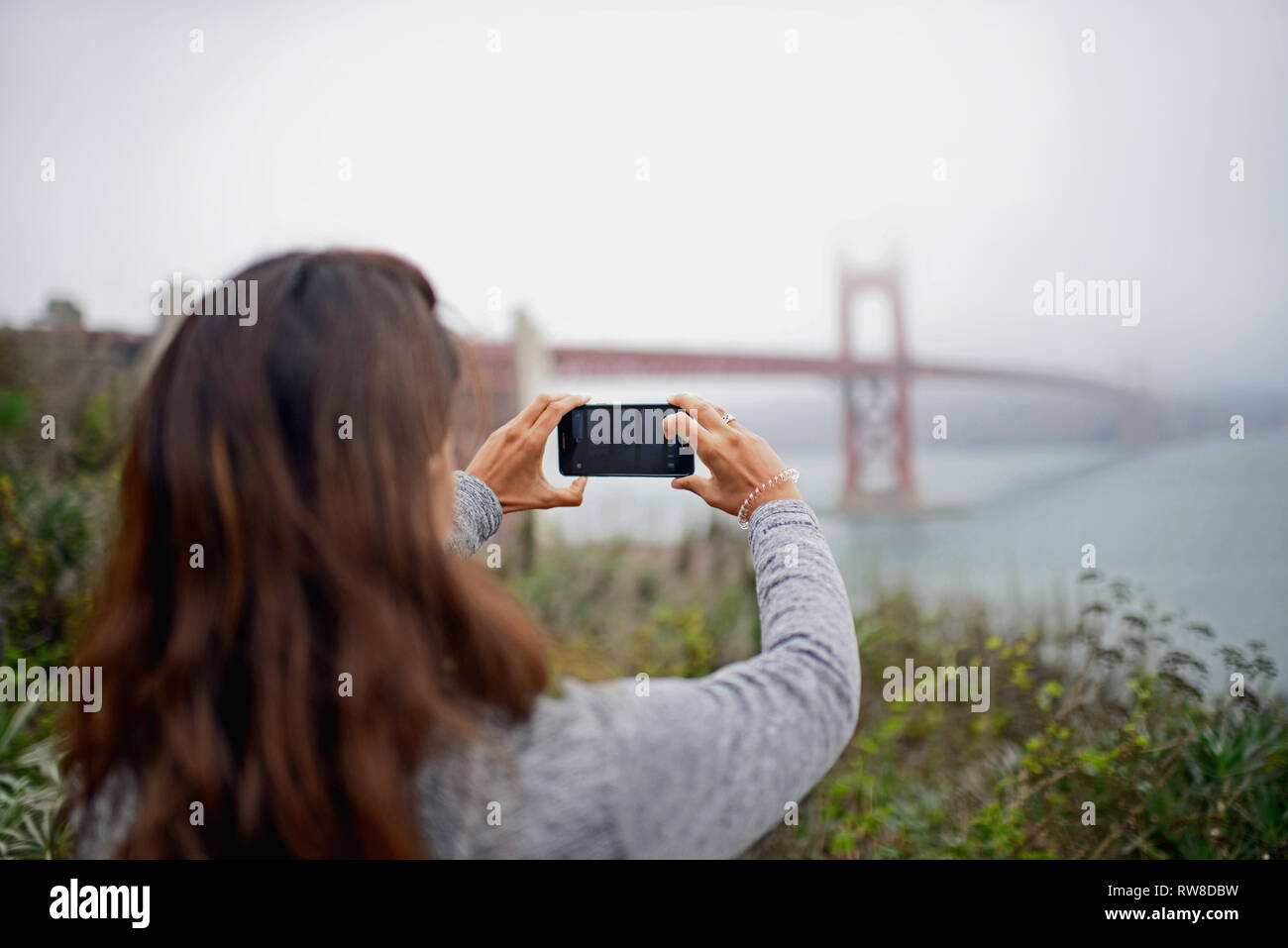 Giovane donna utilizza lo smartphone per fotografare il Golden Gate Bridge di San Francisco. Foto Stock