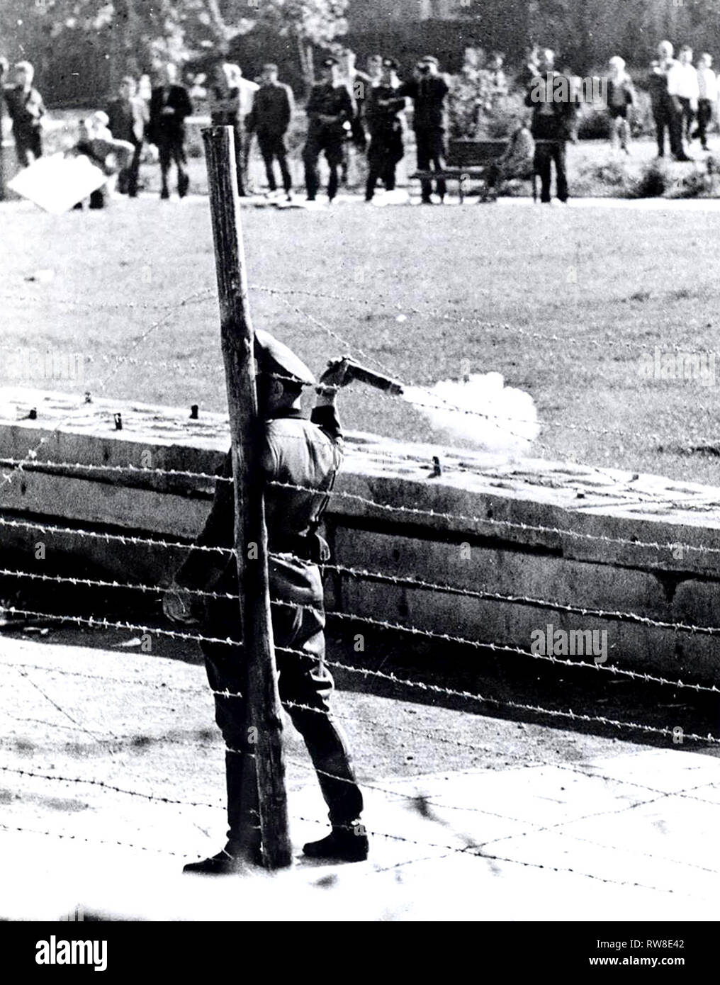 Ottobre 1961 - 'comunista popolare di poliziotti' (Volkspolizist), che si erge tra la recinzione di confine e la parete, si prepara a lanciare una granata Tear-Gas presso un gruppo di West i berlinesi che hanno raccolto sul loro lato del confine per Jeer Guardie rosse Foto Stock