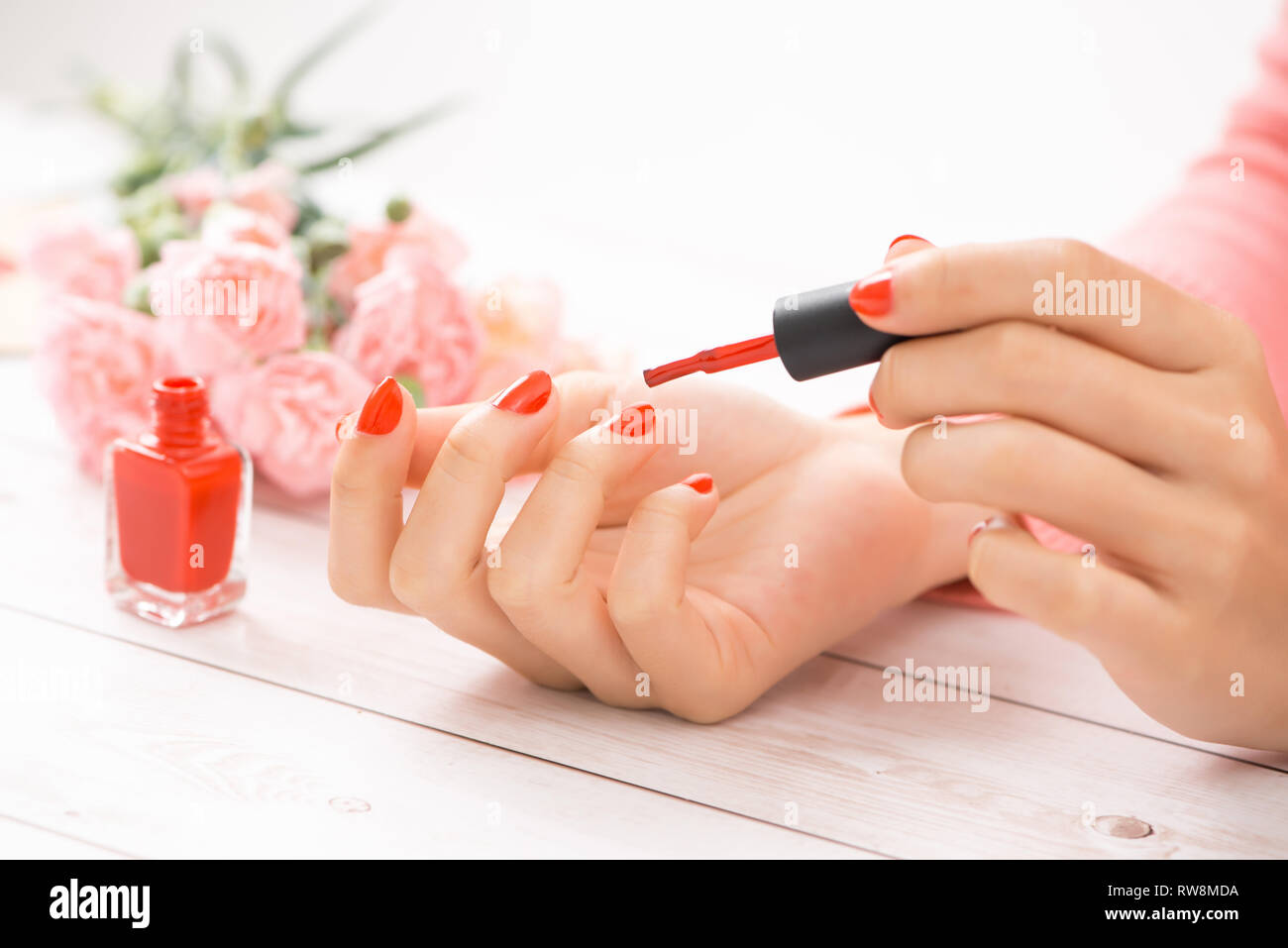 Donna che mantiene la bottiglia di rosso di smalto per unghie nelle sue braccia. Foto Stock