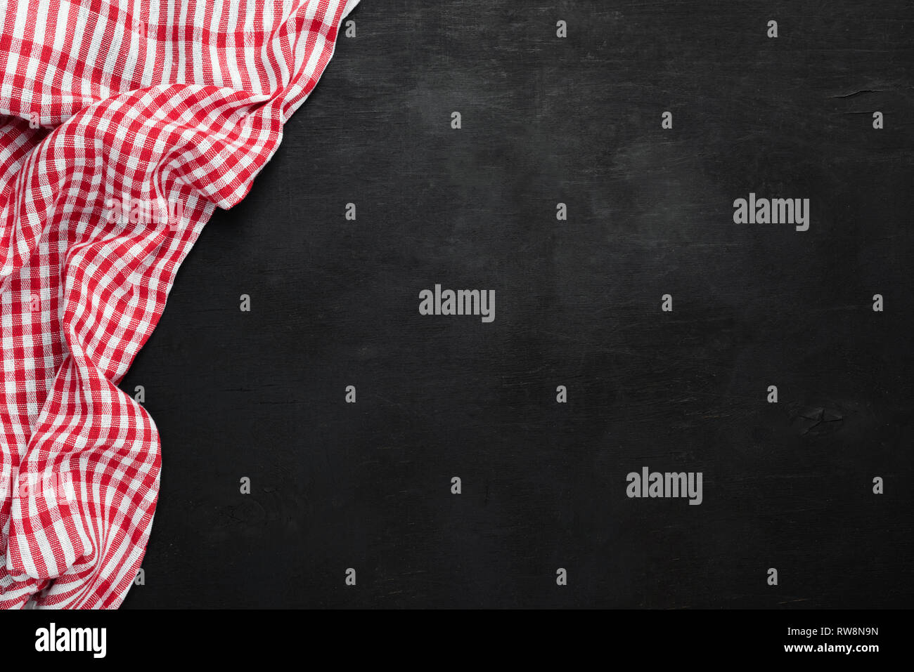Red plaid a scacchi tessili da cucina su sfondo nero, lavagna a fogli mobili o lavagna vecchio. Vista superiore, copia spazio per il testo Foto Stock