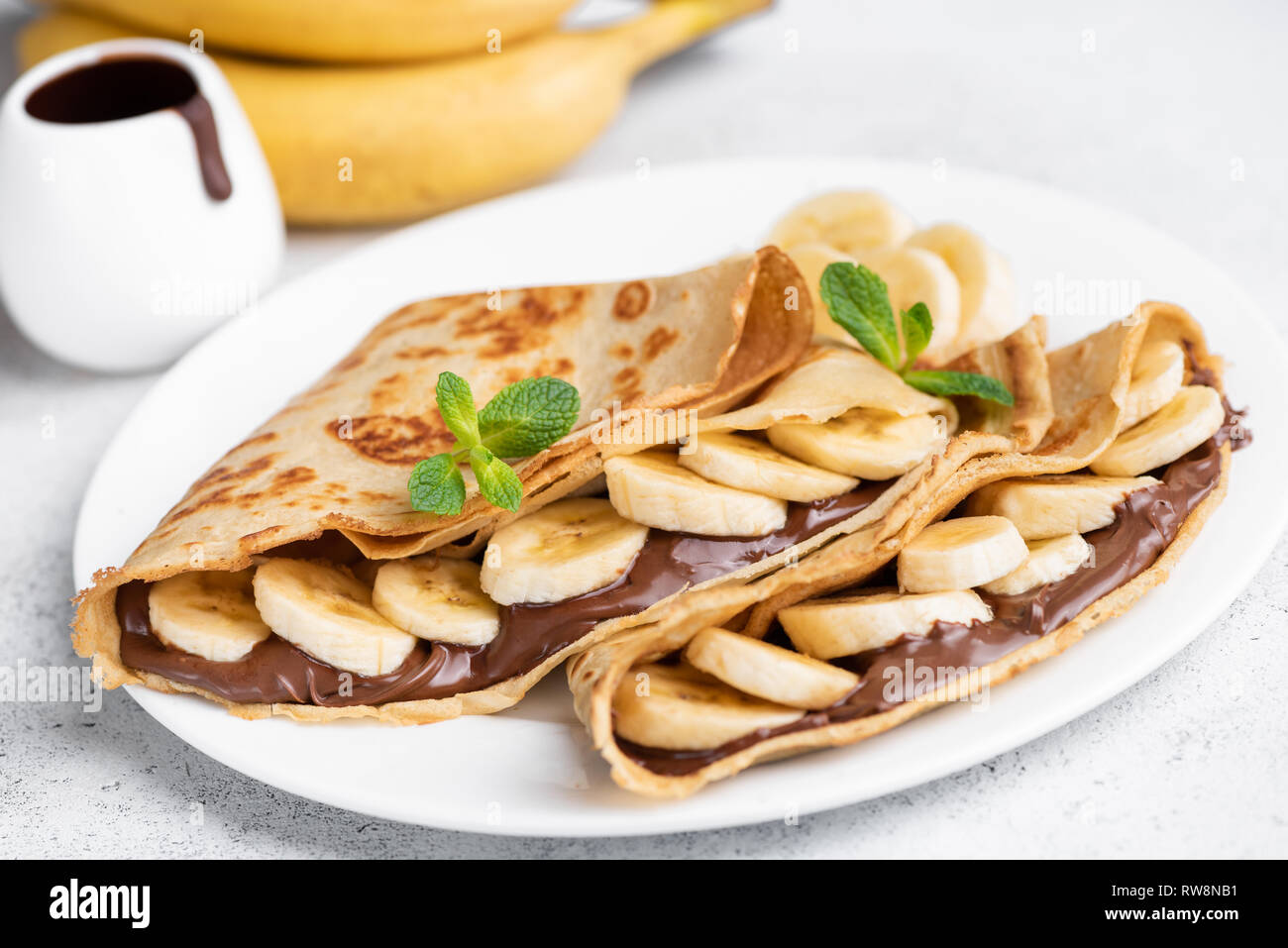 Crepes ripiene di cioccolato da spalmare e banana sulla piastra bianca. Frittelle sottili, blini. Dolce con. Foto Stock