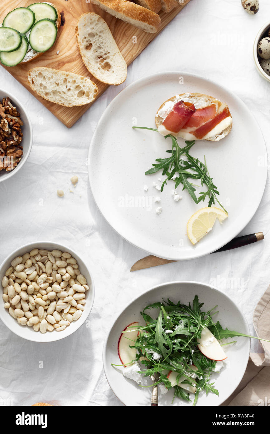 Panini al prosciutto, verdure e insalata di rucola su sfondo chiaro, vista dall'alto. Una sana prima colazione, snack Foto Stock