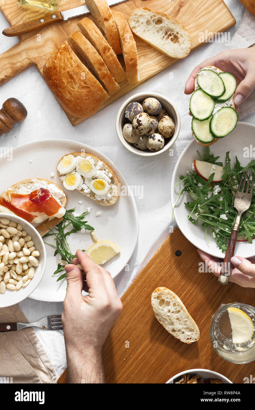 Paio mangiare delizioso e salutare prima colazione o pranzo vista dall'alto. Vari snack, aperitivi, insalata di rucola, panini al prosciutto e verdure Foto Stock