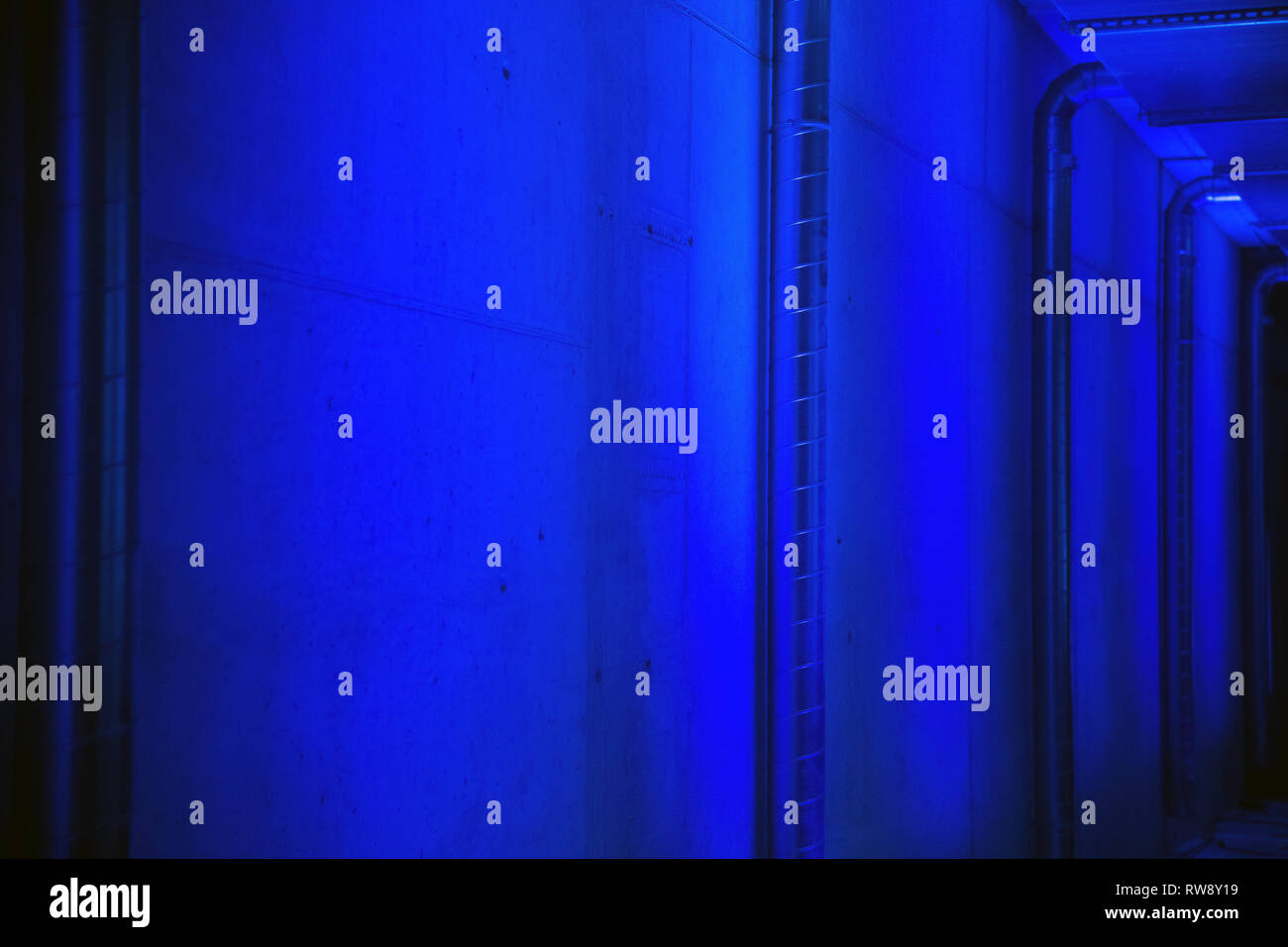 Vista prospettica di tubi di ventilazione e il muro di cemento a garage per il parcheggio illuminato con luce blu Foto Stock