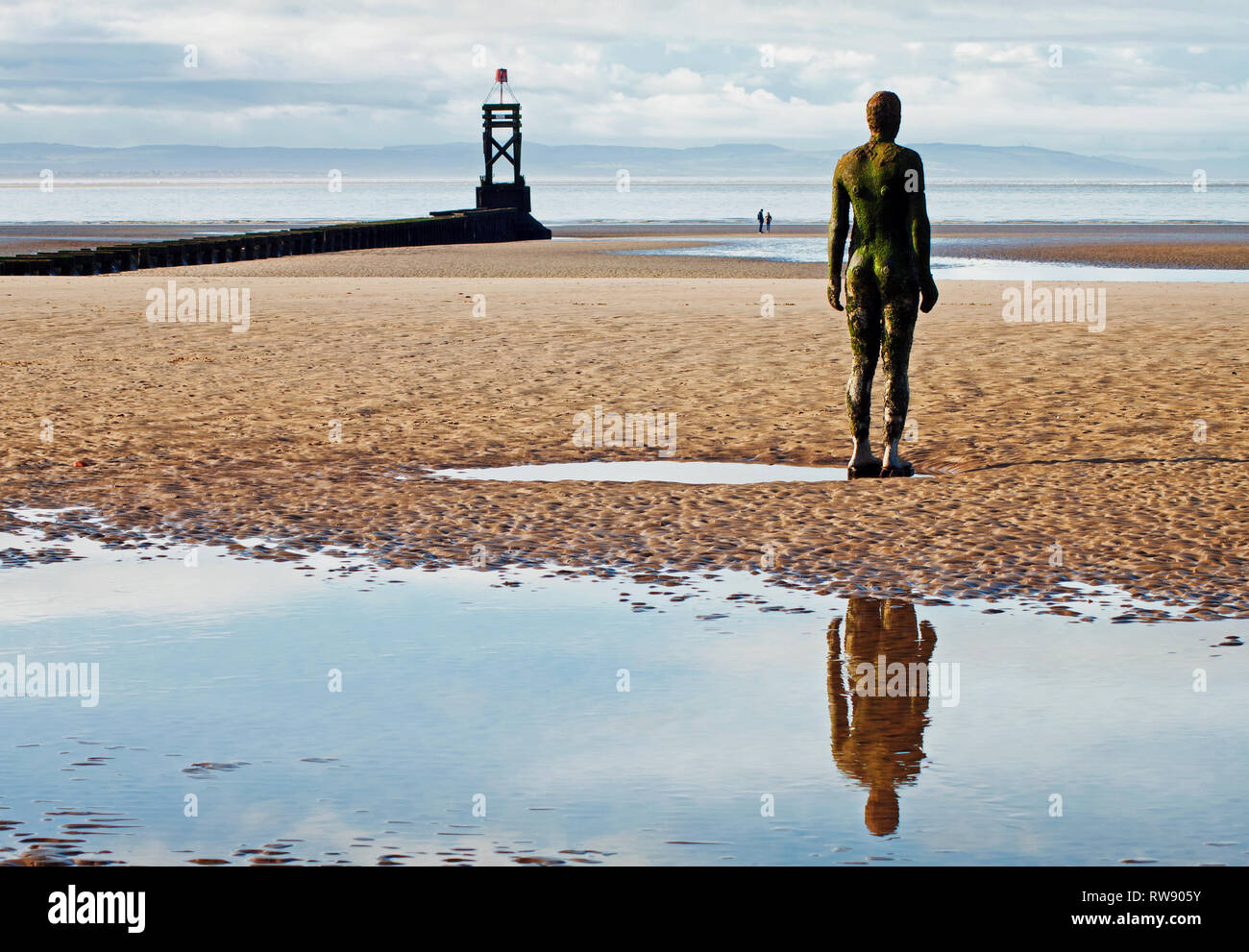 Un uomo di ferro che guarda al mare oltre figure distanti su Crosby Beach, Merseyside Foto Stock