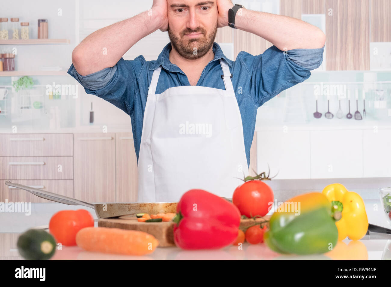 Chef con viso curioso tiene vasi con porridge su sfondo rosso. L'uomo nel  cappello di cuoco e nel grembiule usa i groats. Cucina lavori in cucina  vicino a tavola con verdure e