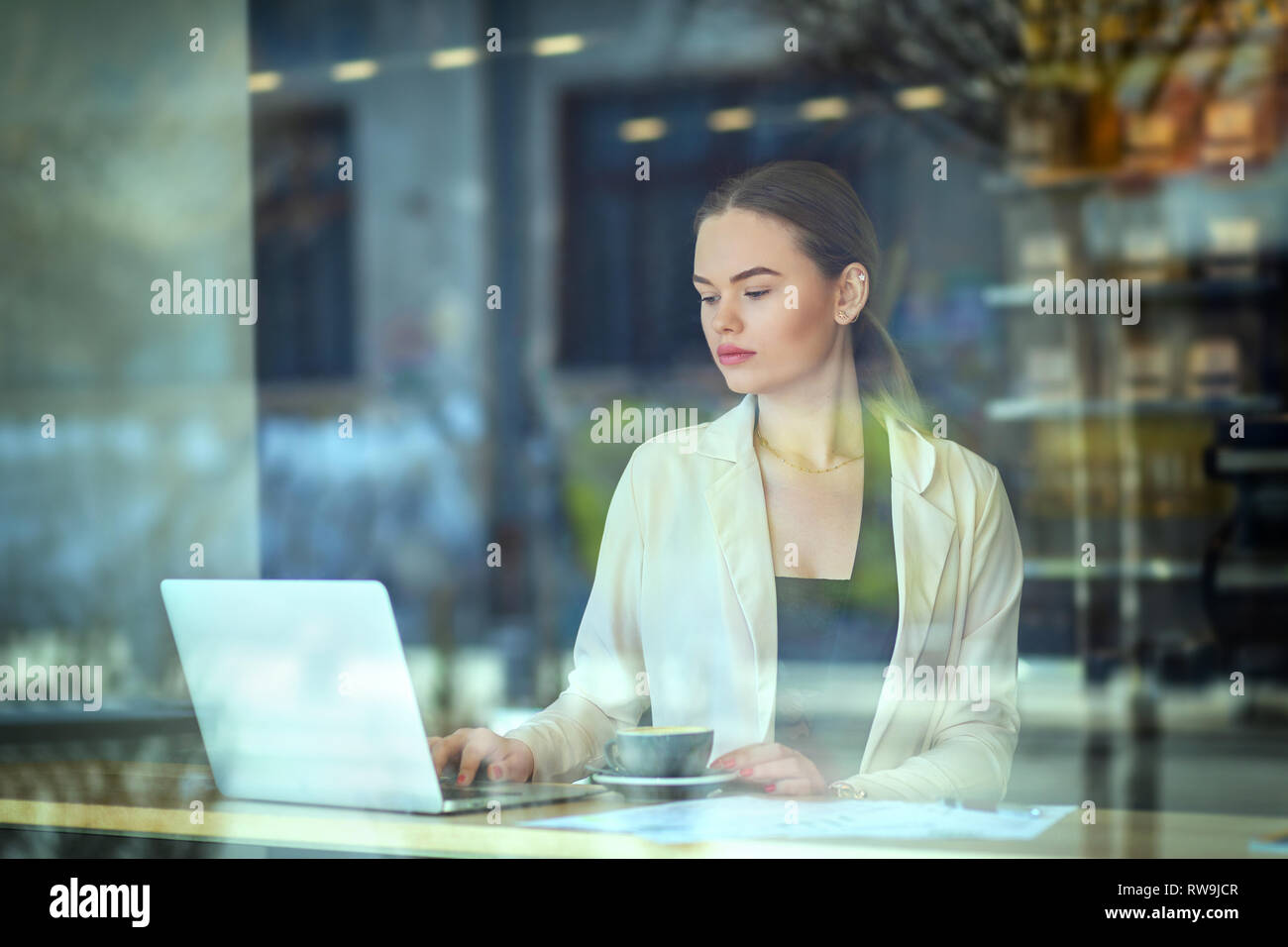 Giovane donna seduta al tavolo della finestra in cafe di bere il caffè mentre si lavora sul computer Foto Stock