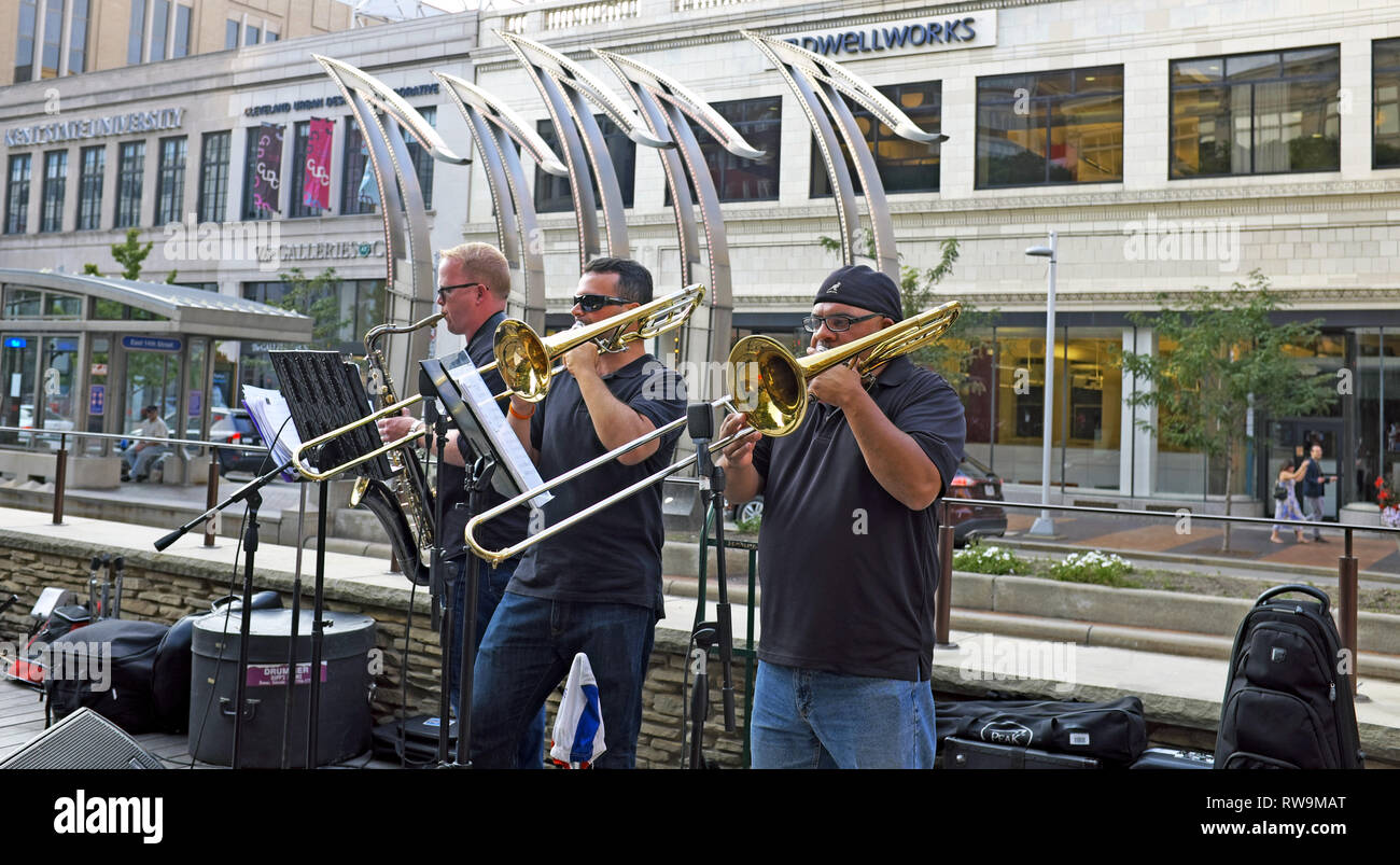 Tre uomini su diversi strumenti a corno suonano nella US Bank Plaza nel Cleveland Playhouse Square Theater District il 14 agosto 2018 a Cleveland. Foto Stock