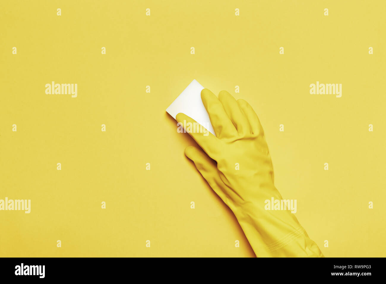 Una mano in una gomma di guanto protettivo con una spugna bianca su sfondo giallo. Il concetto di pulizia. Foto Stock